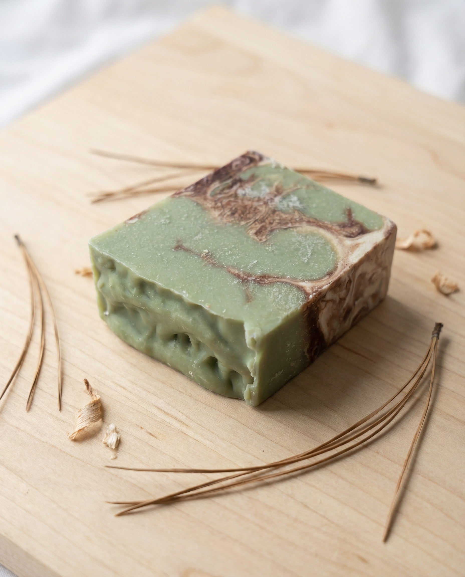 Green soap bar with brown swirls on a wooden surface with pine needles